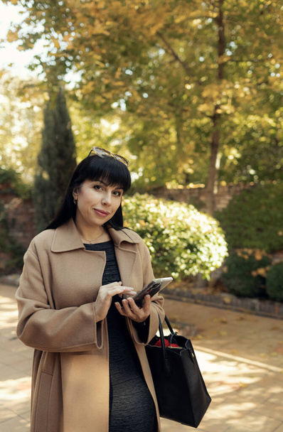 Middle-aged business woman talking on smartphone wearing fashionable fall outdoors. Female stylish model walking city street. Autumn trend, fashion outfit - Photo, Image