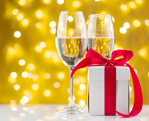 Kieliszki szampana i pudełko prezentów przed lampkami świątecznymi bokeh - Zdjęcie, obraz