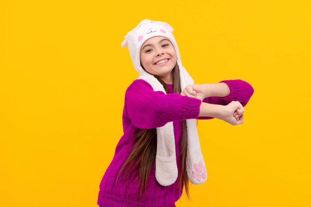 children winter fashion and beauty. teen girl in knitwear. express positive emotion. happy child dancing in earflap hat. kid wear warm clothes on yellow background. - Photo, Image