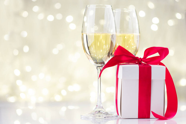 Champagne glasses and gift box in front of Christmas lights bokeh - Photo, Image