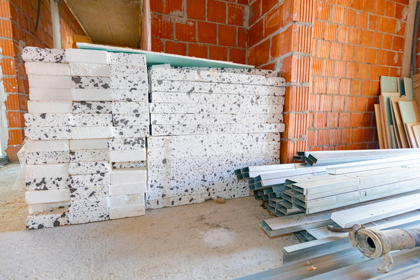 Haufen von Wärmedämmmaterial Styropor und Stapel von neuen verzinkten Metallprofilen für Trockenmauern, die auf dem Boden darauf warten, installiert zu werden. - Foto, Bild