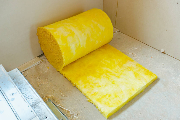 Теплоизоляционный материал, желтый прокат каменной ваты ждет, чтобы быть установлен на стене, интерьер незавершенного нового здания. - Фото, изображение