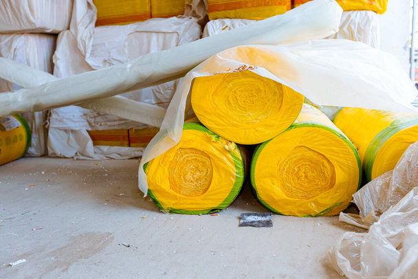Теплоизоляционный материал на складе, желтый прокат каменной ваты ждет, чтобы быть установлен на стене незавершенного нового здания. - Фото, изображение