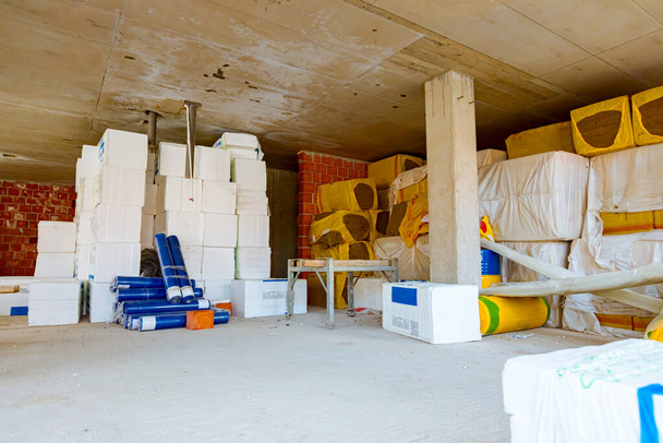 Pakete aus Wärmedämmmaterial, Styropor und in Folie gehüllter gelber Steinwolle warten darauf, an den Wänden im Lager installiert zu werden. - Foto, Bild