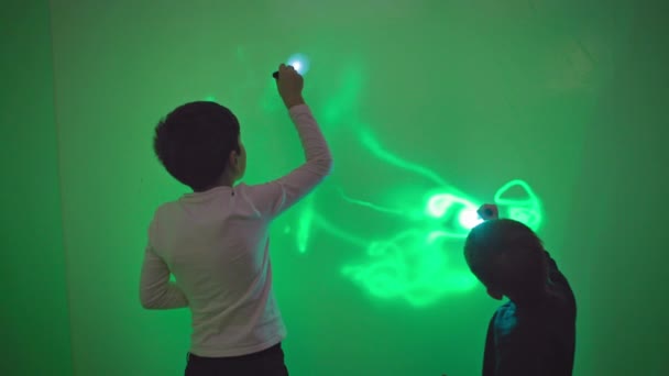 wetenschap en natuurkunde, nieuwsgierige mannelijke kinderen hebben plezier spelen met zaklampen en schilderen patronen op de muur met licht in de groene kamer - Video