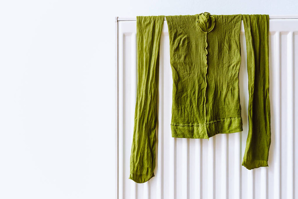 Grüne Nylonstrumpfhosen hängen zum Trocknen an einem Heizkörper. Details aus dem Familienleben, feuchte Nylonstrumpfhosen für Frauen an der Batterie. Konzept des realen Lebens - Foto, Bild
