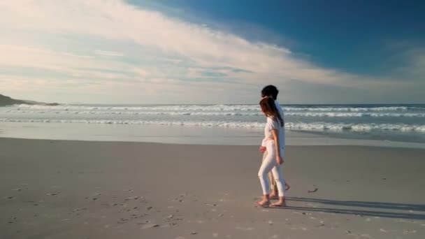 Turista pár fogja a kezét, miközben sétál a nyári strandon Praia de Caion, Spanyolország. Nyomkövető lövés - Felvétel, videó