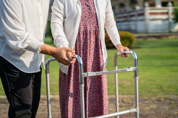 Apua ja hoitoa Aasian vanhempi tai vanhusten vanha nainen käyttää kävelijä vahva terveys kävellessään puistossa onnellista tuoretta lomaa. - Valokuva, kuva