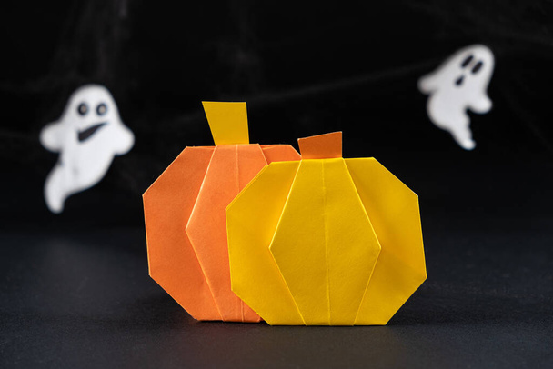 Calabazas de origami hechas de papel para la fiesta de Halloween, sobre el fondo de fantasmas voladores sobre un fondo negro, hazlo tú mismo - Foto, Imagen