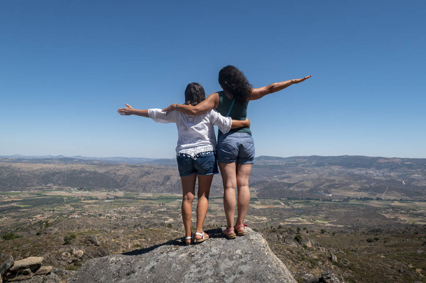 Women tourists on top of a rock with their arms open as a sign of joy and peace while enjoying the scenery around them - Zdjęcie, obraz