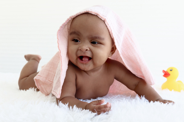 Portret van schattig zes maanden kruipend Afro-Amerikaanse baby bedekt met handdoek na badtijd, gelukkig lachend lief klein meisje kind spelen met gele eend speelgoed, kindertijd en baby care concept. - Foto, afbeelding