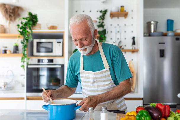 Happy senior man having fun cooking at home - Elderly person preparing health lunch in modern kitchen - Retired lifestyle time and food nutrition concept - Photo, Image