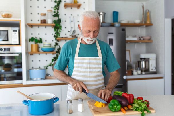 Happy aposentado idoso cozinhar na cozinha. Aposentadoria, conceito de hobby people. Retrato de sorrir homem sênior cortando legumes - Foto, Imagem