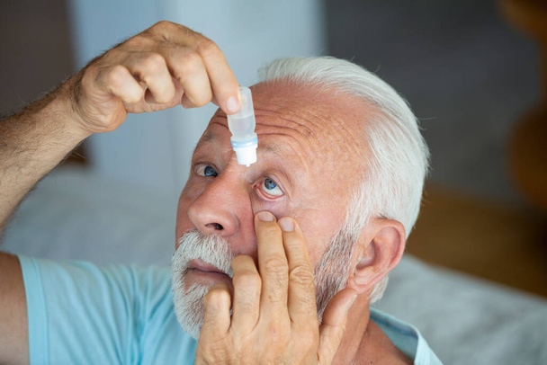 Mann, der Flüssigkeitstropfen in sein Auge gibt, löst Sehprobleme. Senior lässt Augentropfen fallen und heilt seine Augenschmerzen. Sehvermögen und Augenheilkunde Medizin, Senior graue Haare Mann Anwendung Augentropfen. - Foto, Bild