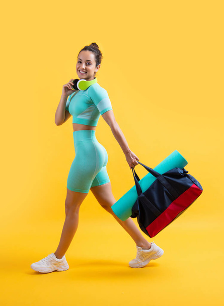 glad fitness woman in sportswear walk with sport bag in studio. fitness woman in workout sportswear isolated on yellow background. fitness and sportswear. - Foto, immagini