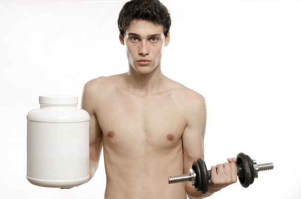 Skinny man traininghis biceps muscle and taking a protein shake. Beautiful teenager lifting a dumbbell.Anorexic young man training to become stronger and using steroids - Photo, Image