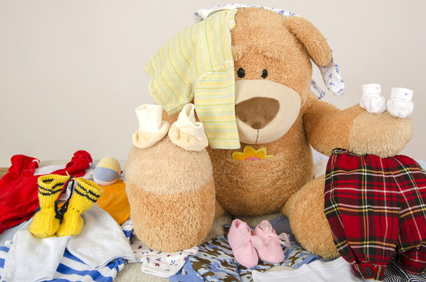 Bear toy on a bed with different colorful new born clothes.Colorful wardrobe of newborn,kids, babies full of all clothes, shoes,accessories and toys - Valokuva, kuva