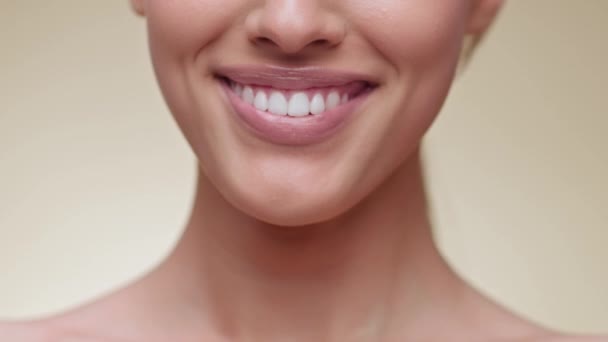 Cuidado dental profesional. Primer plano de mujer joven irreconocible sonriendo a la cámara, demostrando una sonrisa perfecta con dientes blancos sanos, fondo beige del estudio, cámara lenta - Metraje, vídeo