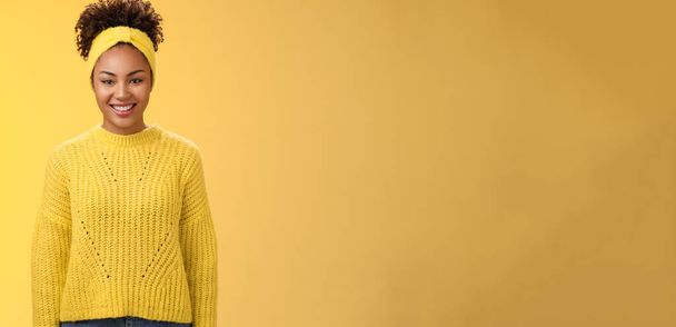 Charismatique amical souriant noir fille bandeau frisé afro coiffure sourire joyeusement excité participer à l'événement universitaire aider debout sortant énergisé fond jaune. - Photo, image