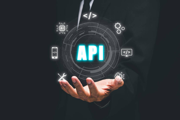 API -アプリケーションプログラミングインターフェイス、オフィスデスクでのVR画面APIアイコンを保持する人の手、ソフトウェア開発ツール、現代技術、インターネットとネットワーキングの概念 - 写真・画像