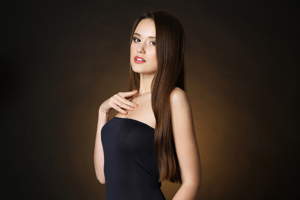 長い髪の暗い茶色の背景に美しい若い女性 - 写真・画像