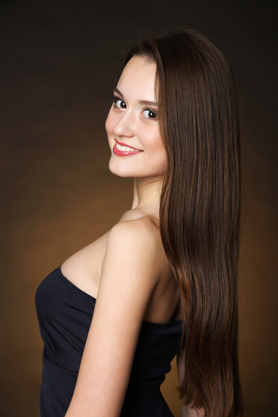 gyönyörű fiatal nő, hosszú haj, sötét barna háttér - Fotó, kép