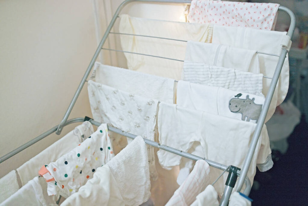 Τα ρούχα του μωρού, οι στολές και τα παντελόνια στεγνώνουν μετά το πλύσιμο. Οργάνωση και καθαρισμός στο παιδικό δωμάτιο. - Φωτογραφία, εικόνα