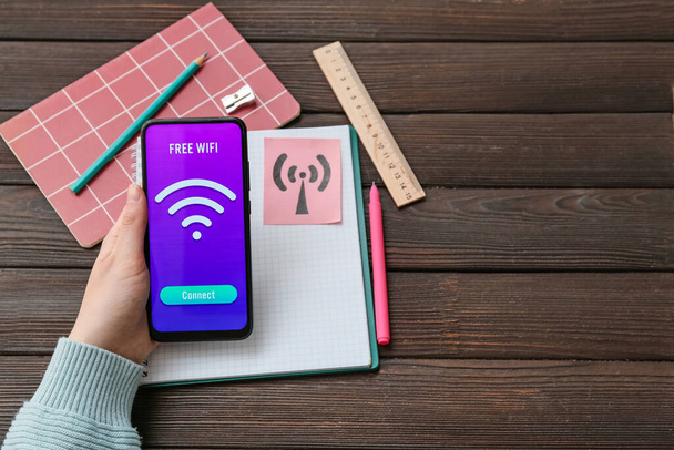 Frau hält Handy mit WiFi-Symbol und Verbindungstaste auf Holzgrund - Foto, Bild