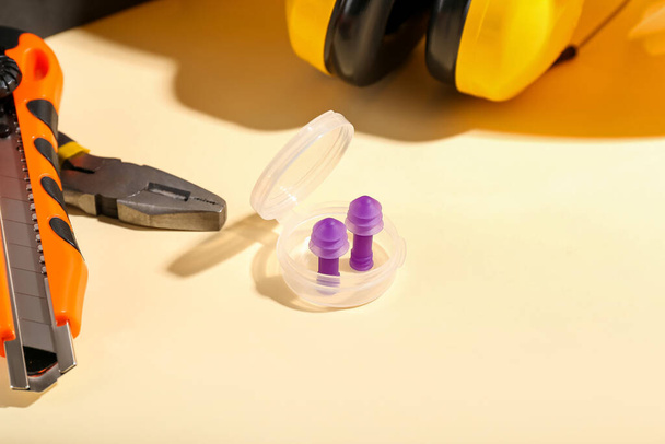 Contenedor de plástico con tapones para los oídos, alicates y cuchillo sobre fondo de color - Foto, Imagen