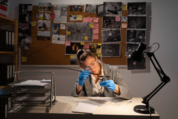 Γυναίκα εγκληματολόγος με γάντια για να εξετάσει γυαλιά αποδεικτικών στοιχείων, επαγγελματικές δεξιότητες των γυναικών στο αστυνομικό τμήμα. Αντιγραφή χώρου - Φωτογραφία, εικόνα