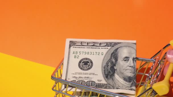 Handschiebender Supermarkt-Einkaufswagen mit 100-Dollar-Schein Geld im Einkaufswagen auf gelbem Hintergrund. Verkaufskorb von US-Dollar-Scheinen. Existenzminimumkonzept: Darlehen, Altersvorsorge ansparen - Filmmaterial, Video