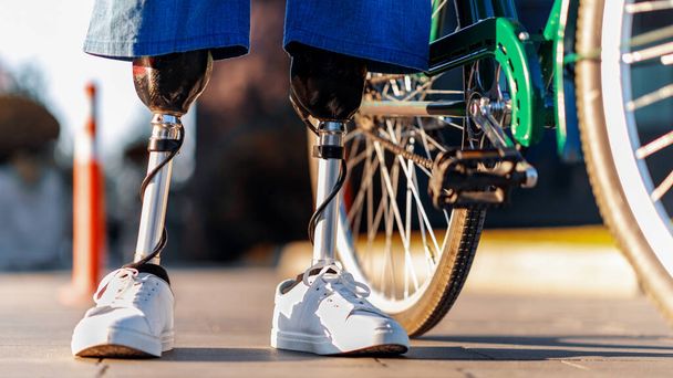 Vista de un hombre con piernas protésicas y zapatillas blancas. De pie junto a su bicicleta - Foto, imagen
