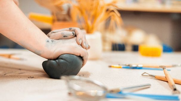 El maestro de la escultura de cerámica que trabaja en un estudio. Amasando un pedazo de arcilla con sus manos. Herramientas sobre la mesa - Foto, imagen