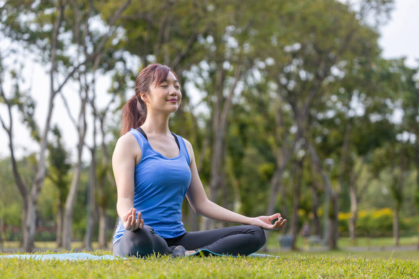 Mujer asiática joven en traje de yoga practicando relajadamente la meditación en el bosque para alcanzar la felicidad desde la paz interior sabiduría para el ejercicio respiratorio, la mente sana y el alma - Foto, imagen