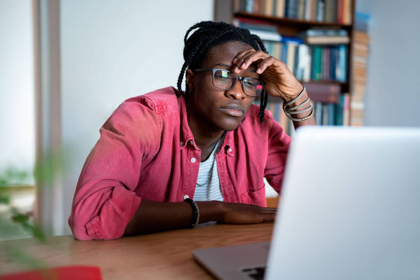 Βαρετός δυστυχισμένος νεαρός Αφρικανός ελεύθερος επαγγελματίας που κοιτάζει την οθόνη του φορητού υπολογιστή δεν μπορεί να συγκεντρωθεί. Αναστατωμένος μαύρος χάνει το κίνητρο ενώ εργάζεται εξ αποστάσεως από το σπίτι, αισθάνεται απαθής προς την εργασία - Φωτογραφία, εικόνα