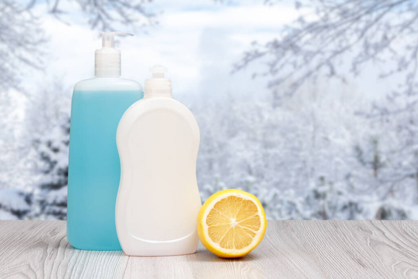 Plastikowe butelki płynu do zmywania naczyń i cytryny z zimowym krajobrazem na tle. Koncepcja mycia i czyszczenia. - Zdjęcie, obraz