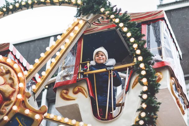 Feliz linda niña preescolar a caballo en el carrusel de la rueda del ferris en la feria o mercado de Navidad, al aire libre. Pequeño niño divirtiéndose en el mercado tradicional de Navidad familiar en Alemania. - Foto, imagen