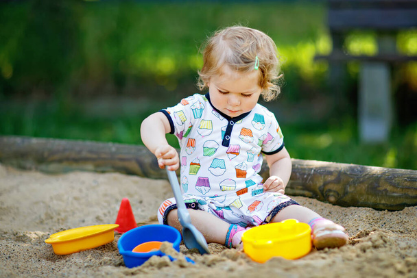 Cute maluch dziewczyna bawiąca się w piasek na placu zabaw. Piękne dziecko w letnich ciuchach bawiące się w słoneczny ciepły letni dzień. Działalność na świeżym powietrzu dla małych dzieci - Zdjęcie, obraz