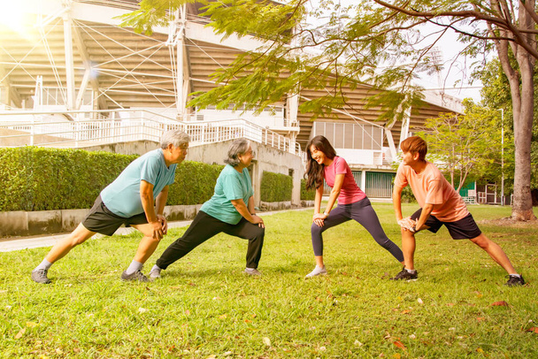 Щаслива азіатська сім'я, старші батьки та дочка похилого віку уважна охорона здоров'я розігрівають гнучкі м'язи легкі вправи перед бігом в саду стадіону в сонячний ранок
. - Фото, зображення