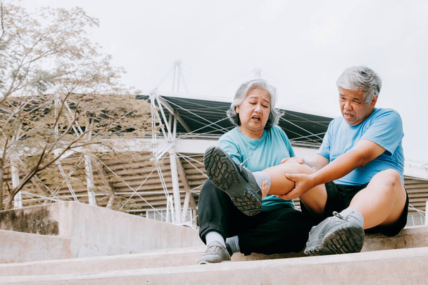 Літній чоловік з болем у правому коліні під час бігу на твердих бетонних сходах спортивного стадіону має серйозний біль у пошкодженому коліні, за яким доглядає його дружина: концепція медичного страхування літніх людей
 - Фото, зображення