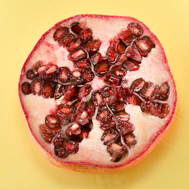 Half of pomegranate on yellow background, square shot - Photo, Image