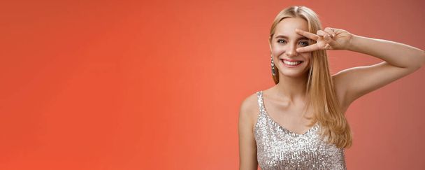 Lifestyle. Joyful carefree attractive confident blond woman in stylish silver dress show disco sign victory peace gesture near eye smiling having fun enjoying awesome party grinning dancing red - Photo, Image