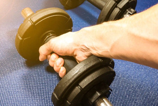 Man takes Heavy black dumbbells lying on the sports mat in the gym. Fitness sport motivation. Happy healthy lifestyle living. Exercises with bars weights. Home sport training. - Photo, Image