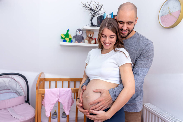 A terhes nő magához ölelte a partnere nagy pocakját. Egy boldog szerető pár, akik a szülésre készülnek.. - Fotó, kép