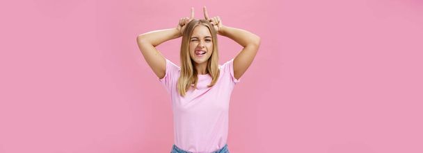 Stubborn girl never let down on dreams. Charming excited and carefree optimistic young woman with tan and fair hair winking showing tongue playfully holding index fingers on head like horns. Body - Photo, Image