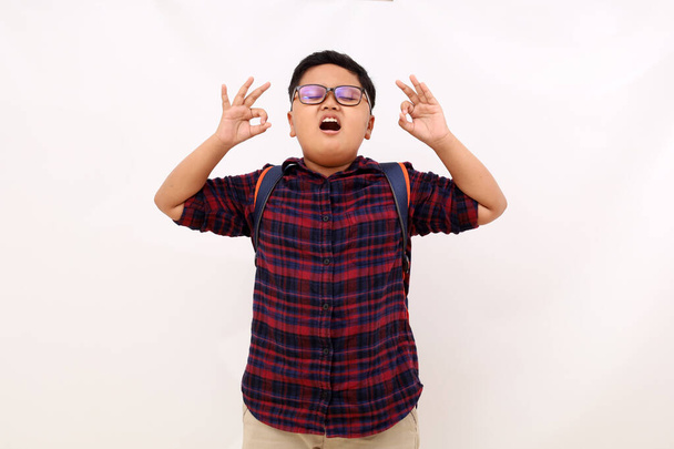 Détendu paisible asiatique écolier garçon méditant avec les yeux fermés. Garder les mains dans le geste Mudra, debout isolé sur fond blanc - Photo, image