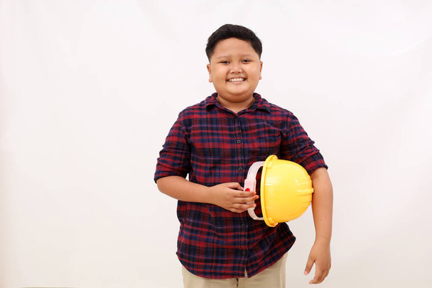 Щасливий азіатський хлопчик стоїть під час носіння інженерного шолома. Концепція прагнень дитини. Ізольовані на білому тлі
 - Фото, зображення