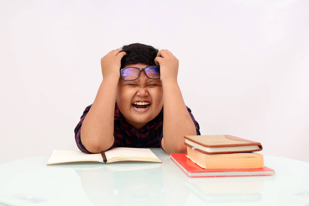 Stressed asian school boy holding his head while doing his homework. Isolado sobre fundo branco - Foto, Imagem