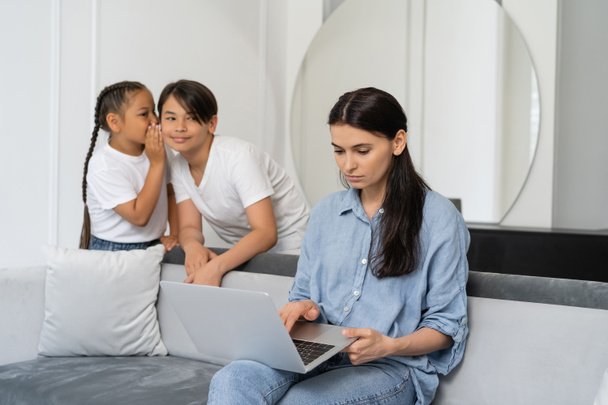 madre usando laptop cerca asiático niños hablando en casa  - Foto, Imagen