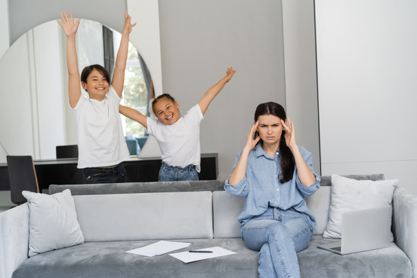 Excited asian kids standing near tired mother and laptop at home  - Foto, afbeelding